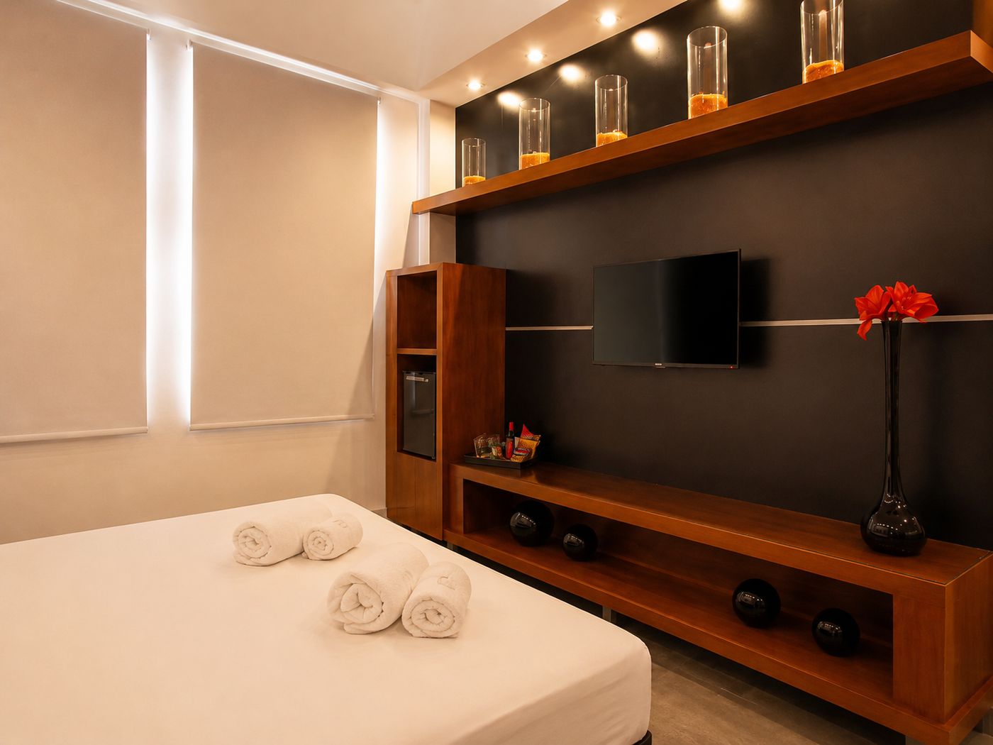 Categoría Estudio: cama y panel de TV en madera con frigobar y velas.