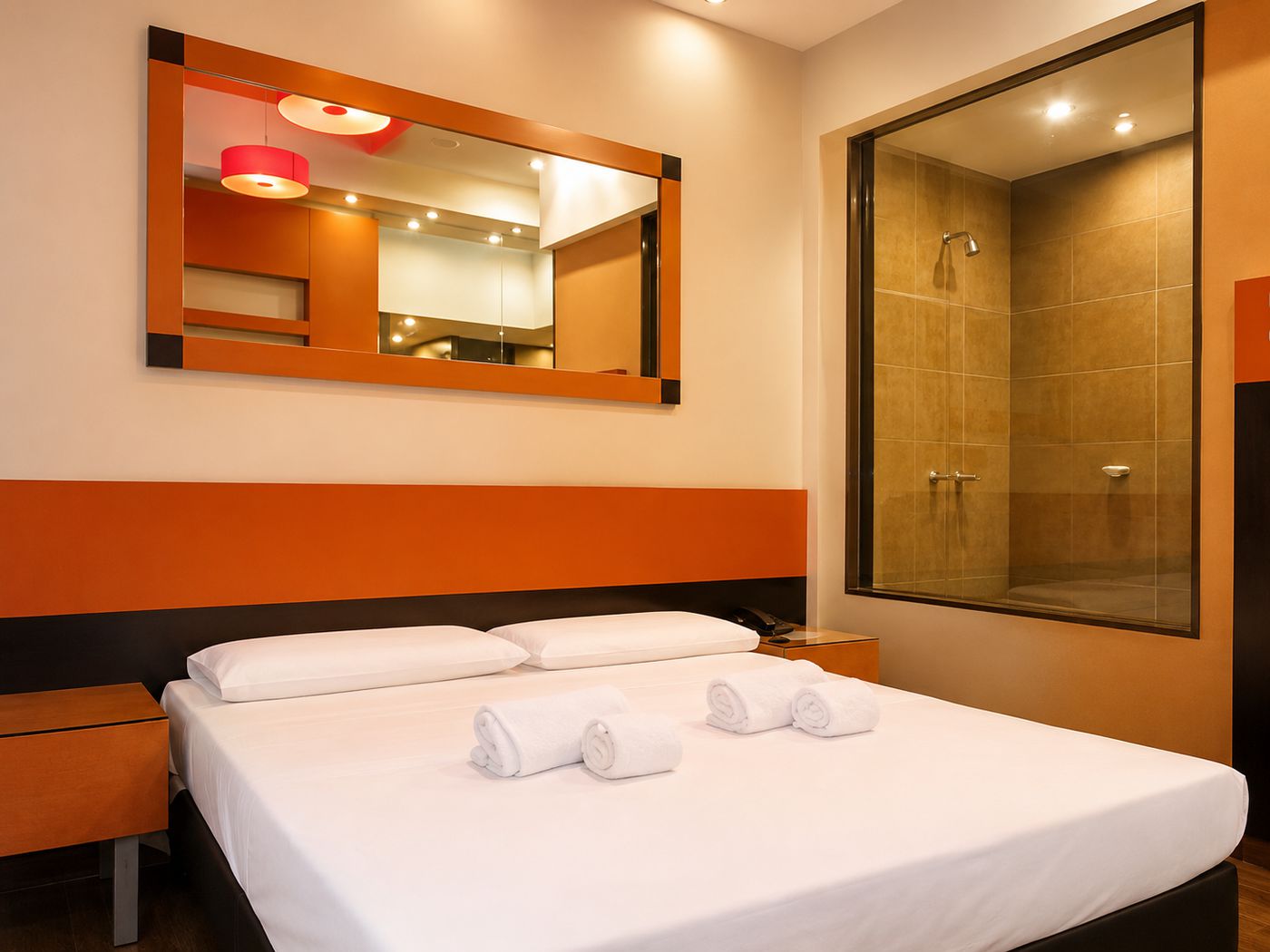 Categoría Suite: habitación en tonos naranjas con espejo y ducha vidriada.